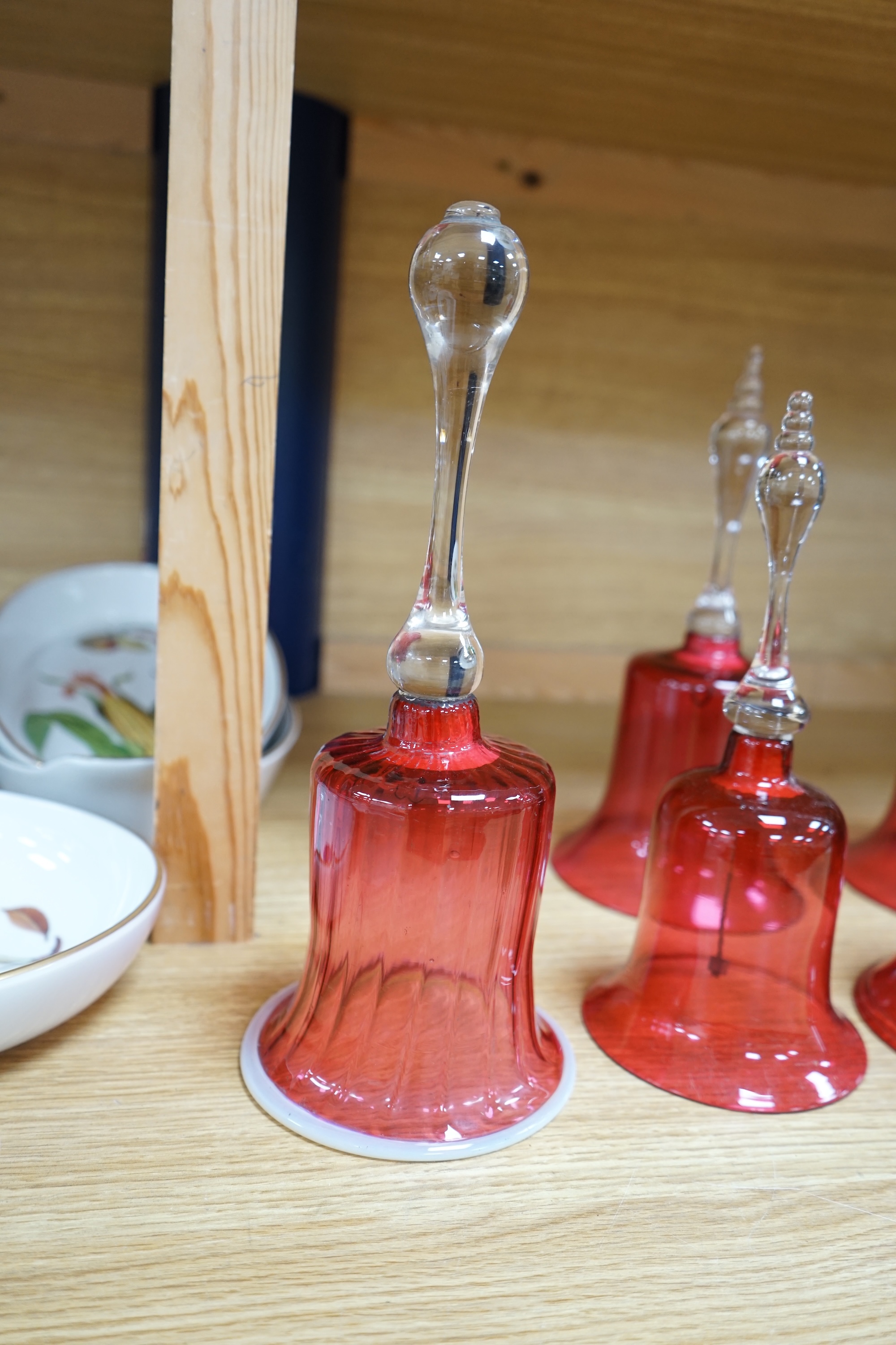 Seven 19th century cranberry glass hand bells, various sizes, largest 30.5cm high. Condition - fair